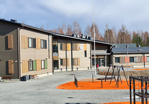 Koulurakennus Iisalmen Mansikkaniemellä, pihalla kiipeilytelineitä ja pelikenttiä.