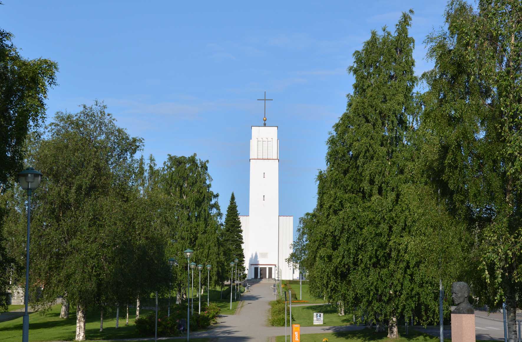 Valkea kirkkorakennus koivukujan päässä mäellä Iisalmessa.