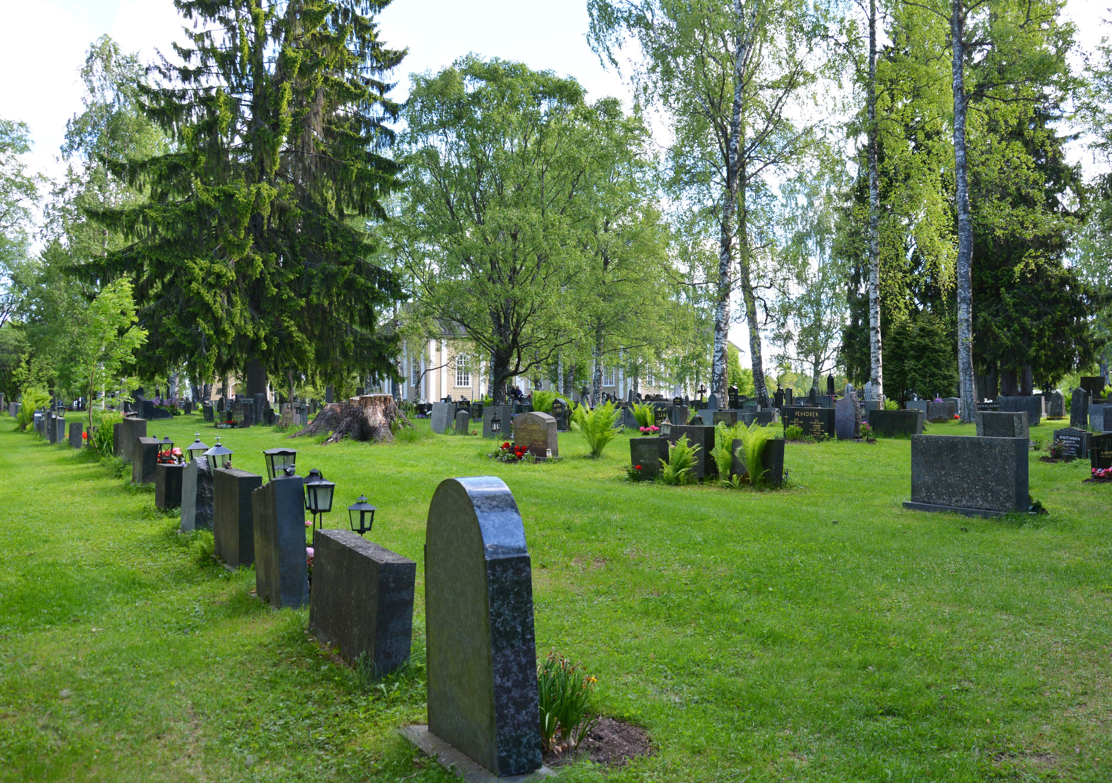 etualalla hautarivi ja nurmikkoa, takana lehdessä olevia puita, joiden takaa näkyy Kustaa Aadolfin kirkko