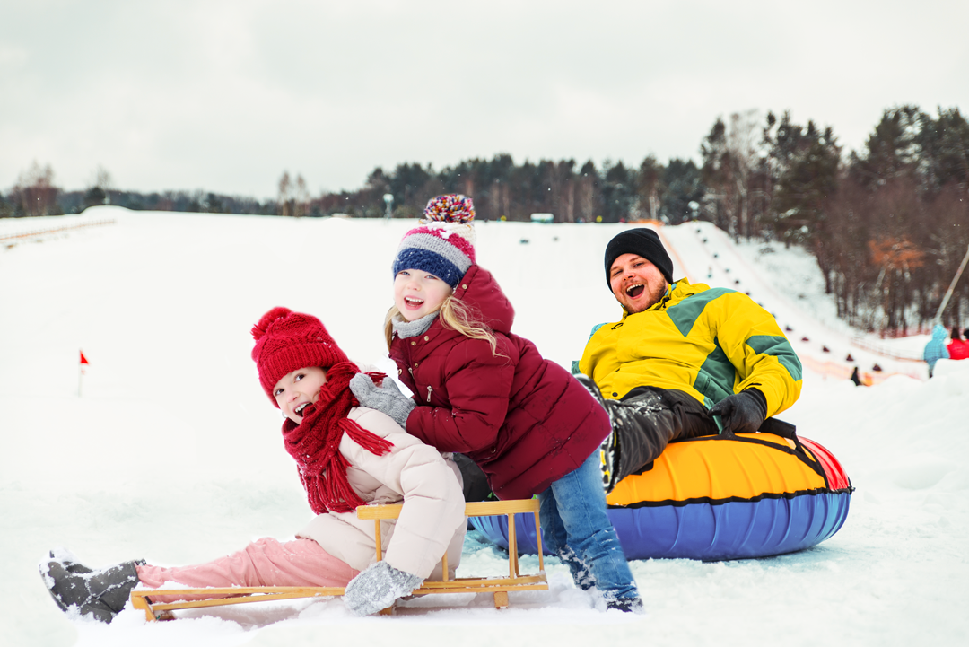 Lapsia ja nuoria laskemassa mäkeä kelkalla ja donitsilla.