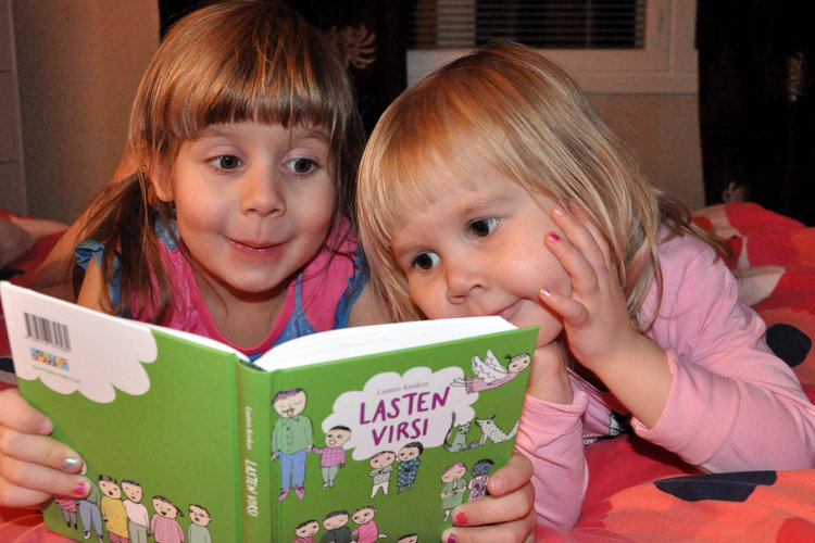 Kaksi pientä tyttöä lukemassa lasten virsikirjaa silmät suurina innostuksesta.