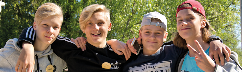 Kuvassa neljä iloista nuorta miestä kädet toistensa olkapäillä. Rippileiri on juuri alkanut.