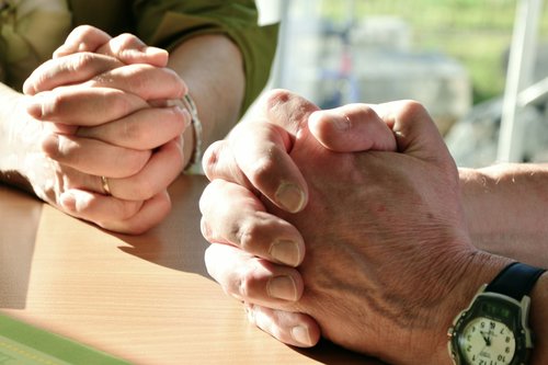 Kaksi henkilöä rukoilee kädet ristissä.