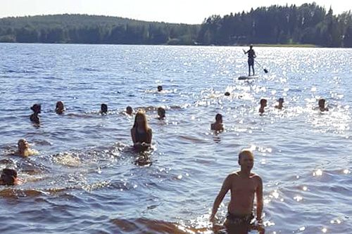 Iso joukko nuoria leiriläisiä on uimassa. Aurinko paistaa.