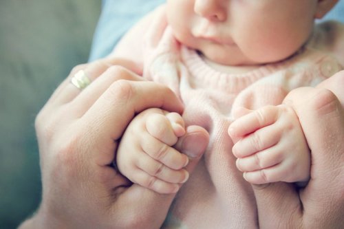 Aikuinen pitelee vauvan käsiä.